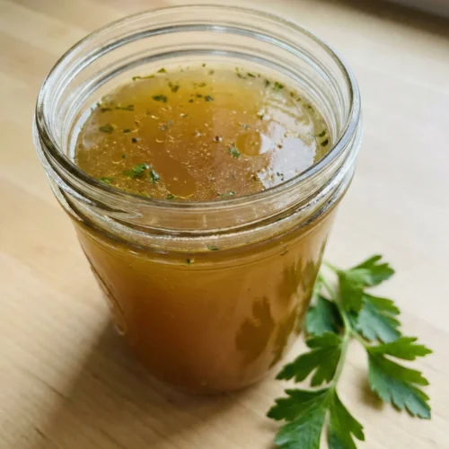 A large glass jar filled with finished golden chicken broth on a kitchen counter.