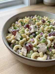 A spoonful of chicken pasta salad being lifted from a bowl, ready to eat.