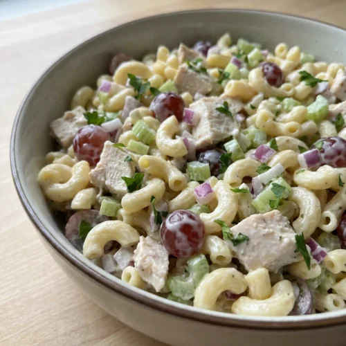 A spoonful of chicken pasta salad being lifted from a bowl, ready to eat.