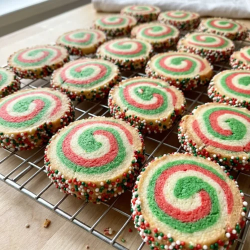 An overhead view of a baking sheet with freshly baked, colorful pinwheel cookies.