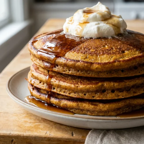 A tall stack of fluffy gingerbread pancakes with whipped cream on top.