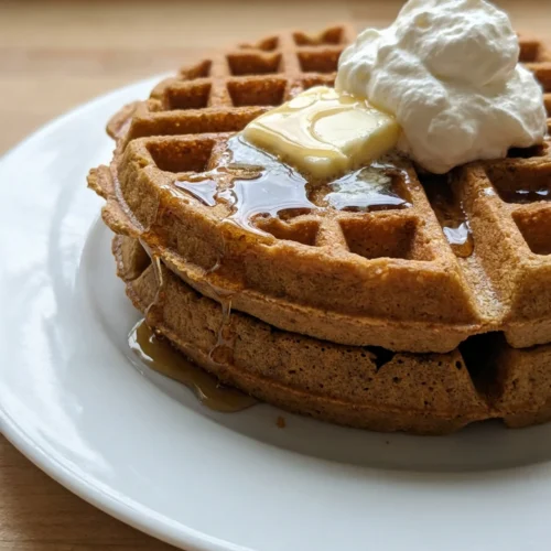 A close-up of two gingerbread waffles on a white plate, topped with whipped cream.