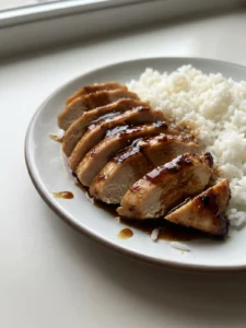 A white plate with sliced chicken breast, honey garlic sauce, and a side of white rice.