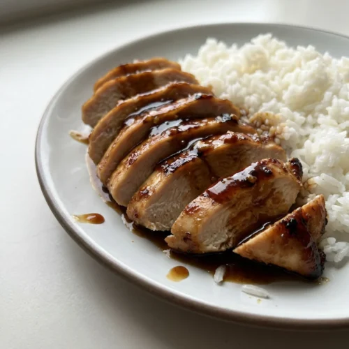 A white plate with sliced chicken breast, honey garlic sauce, and a side of white rice.