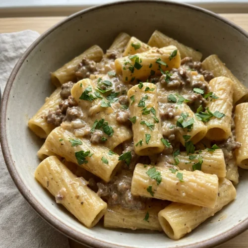 A close-up of creamy beef pasta in a white bowl.