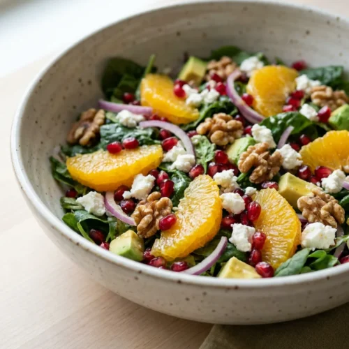 A bright, colorful pomegranate orange salad with feta in a shallow white serving bowl.