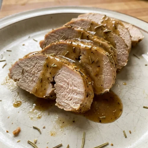 A white plate with sliced turkey tenderloin, drizzled with pan sauce and garnished with parsley.